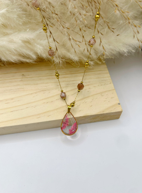 Naszyjnik handmade – przezroczysta, kroplowa zawieszka z żywicy z zatopionymi różowymi suszonymi kwiatami na pozłacanym łańcuszku zdobionym fasetowanymi kamieniami słonecznymi, na miękkim, beżowym tle. Naszyjnik handmade – przezroczysta, kroplowa zawieszka z żywicy z zatopionymi różowymi suszonymi kwiatami na pozłacanym łańcuszku zdobionym fasetowanymi kamieniami słonecznymi, na miękkim, beżowym tle.