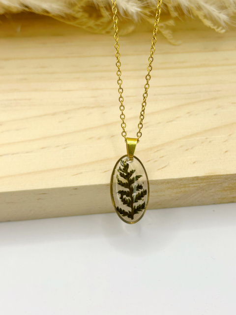 Naszyjnik handmade – owalna zawieszka z żywicy z zatopioną zieloną paprotką leśną na subtelnym pozłacanym łańcuszku, na naturalnym, drewnianym tle. Naszyjnik handmade – owalna zawieszka z żywicy z zatopioną zieloną paprotką leśną na subtelnym pozłacanym łańcuszku, na naturalnym, drewnianym tle.