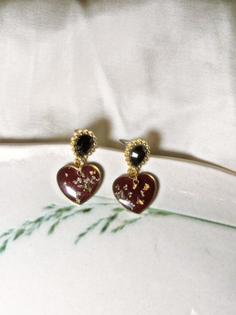 Wiszące kolczyki w kształcie serduszek z kolorowymi kwiatami zatopionymi w żywicy, bigiel ozdobiony czarną cyrkonią.