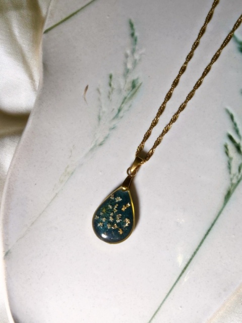 Naszyjnik z żywicy w kształcie kropli z kolorowymi kwiatami na tle butelkowej zieleni. łańcuszek typu singapurka.